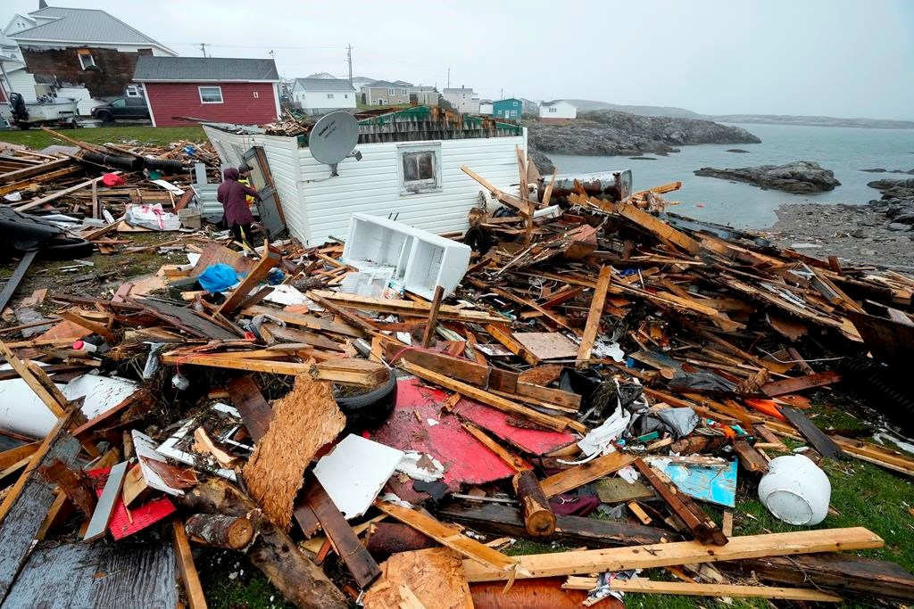 A resident and search and rescue worker examine the destroyed remains of a home in Port aux Basques, N.L., Monday, Sept.26, 2022. Three tupperware bins hold all that remains of Peggy Savery's life and home since post-tropical storm Fiona ravaged her Newfoundland community and swept away most of her possessions last September. THE CANADIAN PRESS/Frank Gunn