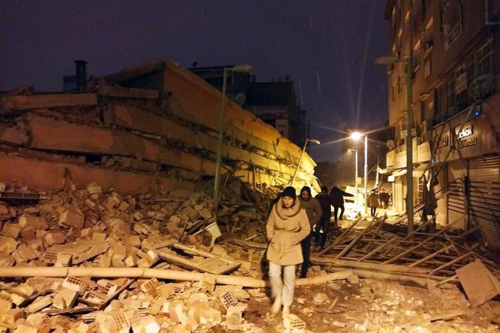 People walk next to buildings destroyed by an earthquake in Malatya, Turkey, Monday, Feb. 6, 2023. A powerful quake has knocked down multiple buildings in southeast Turkey and Syria and many casualties are feared. (DIA images via AP)