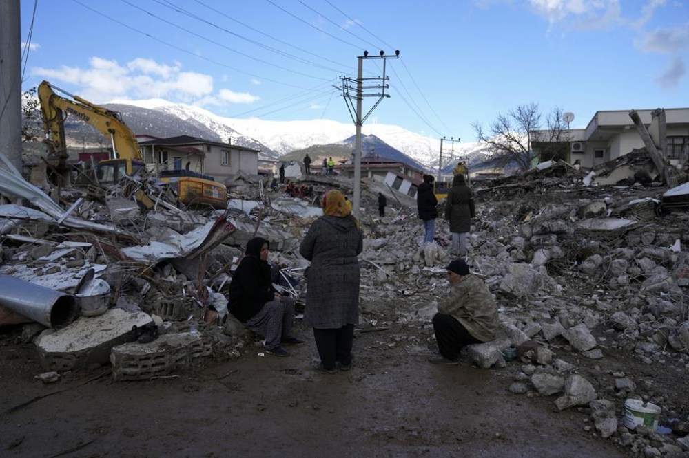 People sit on the rubble as emergency rescue teams search for people under the remains of destroyed buildings in Nurdagi town on the outskirts of Osmaniye city southern Turkey, Tuesday, Feb. 7, 2023. A powerful earthquake hit southeast Turkey and Syria early Monday, toppling hundreds of buildings and killing and injuring thousands of people. (AP Photo/Khalil Hamra)
