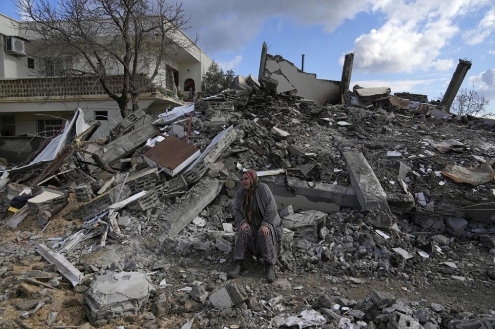 A woman sits on the rubble as emergency rescue teams search for people under the remains of destroyed buildings in Nurdagi town on the outskirts of Osmaniye city southern Turkey, Tuesday, Feb. 7, 2023. A powerful earthquake hit southeast Turkey and Syria early Monday, toppling hundreds of buildings and killing and injuring thousands of people. (AP Photo/Khalil Hamra)