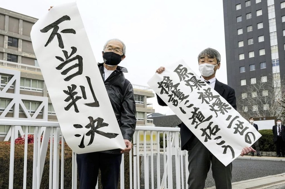 Plaintiff Katsuhiro Hirano, right, and unidentified lawyer for the plaintiffs display signs after a judgement at Hiroshima District Court in Hiroshima, western Japan Tuesday, Feb. 7, 2023. The banners read