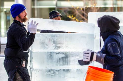 Nate McKeough (left) stacks ice blocks as Anna Sandova adds water between the layers in preparation for ice carving at True North Square on Tuesday. (Mikaela MacKenzie / Winnipeg Free Press)