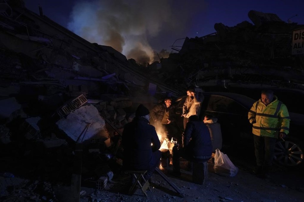 People warm up with fire in front of destroyed buildings in Antakya, southern Turkey, Wednesday, Feb. 8, 2023. With the hope of finding survivors fading, stretched rescue teams in Turkey and Syria searched Wednesday for signs of life in the rubble of thousands of buildings toppled by a catastrophic earthquake. (AP Photo/Khalil Hamra)