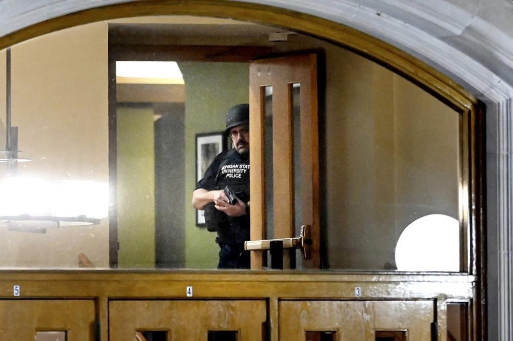 A police officer, with his gun drawn, is seen through the window at an entrance at the Michigan State University Union following shootings on campus on Monday, Feb. 13, 2023, in East Lansing, Mich. (Nick King/Lansing State Journal via AP)