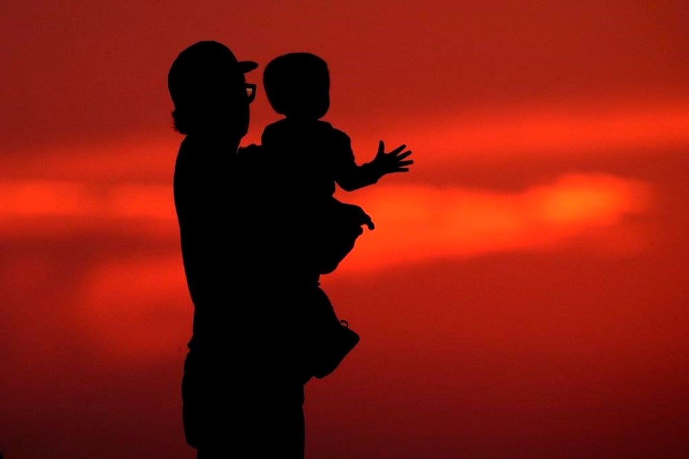 Pandemic benefits rolled out to cushion the blow of COVID-19 lockdowns had the unintended consequence of dramatically reducing poverty levels, and now, a group is calling on the federal government to build on that success. A silhouette against the sky of a man holding a child in Kansas City, Mo., Friday, June 26, 2020. THE CANADIAN PRESS/AP-Charlie Riedel