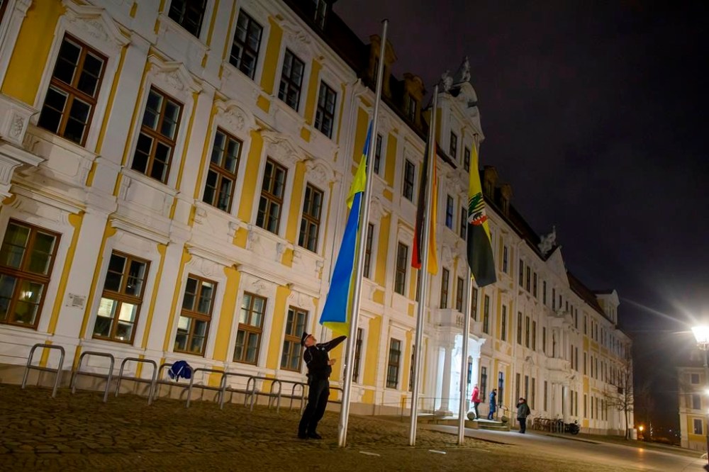 A policeman raises the flag of Ukraine in front of the state parliament of Saxony-Anhalt in Magdeburg, Germany Friday, Feb. 24, 2023. (Klaus-Dietmar Gabbert/dpa via AP)