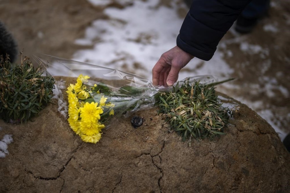 A man lays flowers on the grave of a relative during a memorial service to mark the one-year anniversary of the start of the Russia Ukraine war, in a cemetery in Bucha, Ukraine, Friday, Feb. 24, 2023. (AP Photo/Emilio Morenatti)
