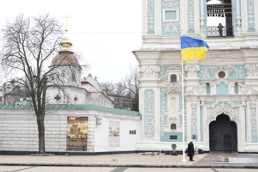 A woman stands under the Ukrainian flag in front of St. Sophia's Cathedral in Kyiv, Ukraine, Friday, Feb. 24, 2023. Ukraine's president pledged to push for victory in 2023 as he and other Ukrainians on Friday marked the somber first anniversary of the Russian invasion that he called