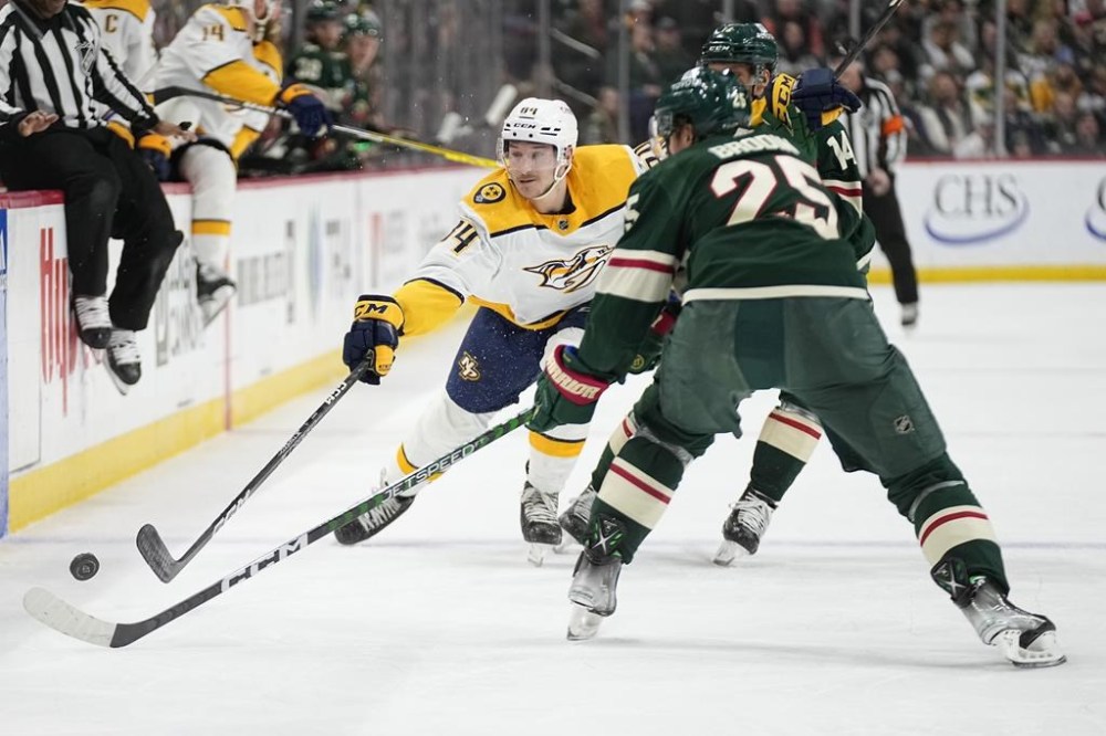 Nashville Predators left wing Tanner Jeannot, left, reaches for the puck next to Minnesota Wild defenseman Jonas Brodin (25) during the second period of an NHL hockey game Sunday, Feb. 19, 2023, in St. Paul, Minn. (AP Photo/Abbie Parr)