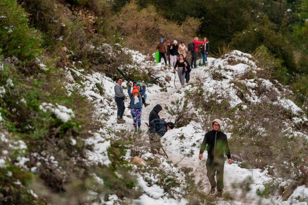 People walk along a trail partially covered in snow at the Deukmejian Wilderness Park, a rugged 709-acre site in the foothills of the San Gabriel Mountains, at the northernmost extremity of Glendale, Calif., Sunday, Feb. 26, 2023. (AP Photo/Damian Dovarganes)