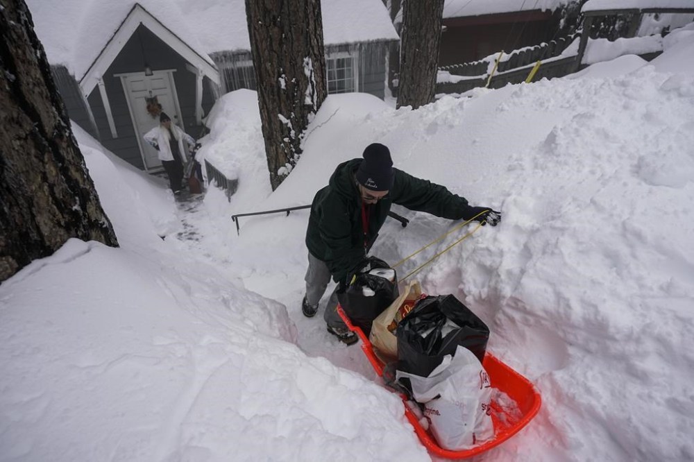 Angie Gourirand walks down the snow-covered steps of her home with groceries on a sled in Running Springs, Calif., Tuesday, Feb. 28, 2023. Beleaguered Californians got hit again Tuesday as a new winter storm moved into the already drenched and snow-plastered state, with blizzard warnings blanketing the Sierra Nevada and forecasters warning residents that any travel was dangerous. (AP Photo/Jae C. Hong)
