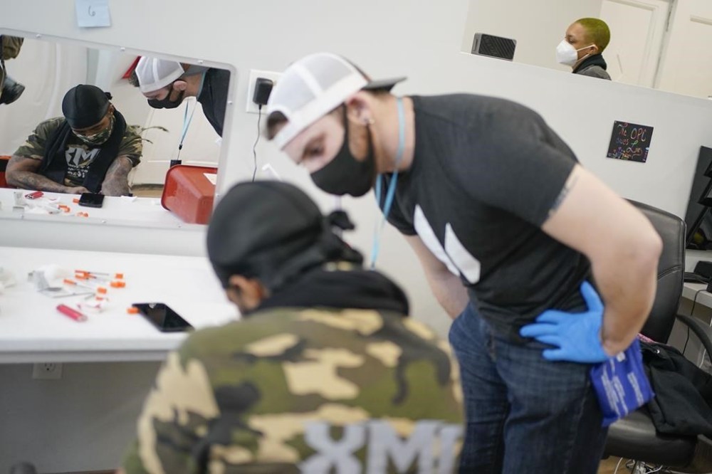 FILE - Brian Hackel, right, an overdose prevention specialist, helps Steven Baez, a client suffering addiction, find a vein to inject intravenous drugs at an overdose prevention center, OnPoint NYC, in New York, Feb. 18, 2022. Across the U.S., drug overdoses killed an estimated 100,000 people in 2021, according to federal health officials. That has pushed lawmakers in Colorado, New Mexico and Nevada to consider joining New York in allowing what are often called “overdose prevention centers