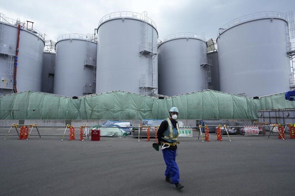 FILE - A worker helps direct a truck driver as he stands near tanks used to store treated radioactive water after it was used to cool down melted fuel at the Fukushima Daiichi nuclear power plant, run by Tokyo Electric Power Company Holdings (TEPCO), in Okuma town, northeastern Japan, on March 3, 2022. Head of Japan’s tsunami-wrecked Fukushima Daiichi nuclear power plant says details of the damages inside reactors are only beginning to unravel 12 years after the meltdowns, making it difficult to foresee what the place looks like even 30 years from now. (AP Photo/Hiro Komae, File)