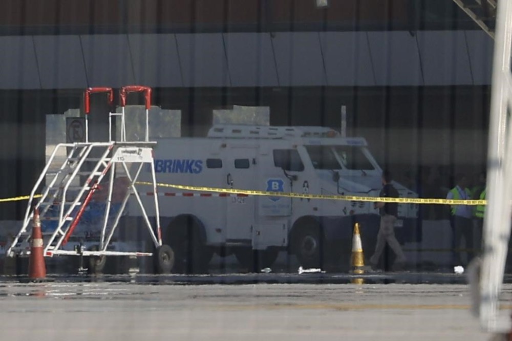 Photographed through a fence, an armored truck is surrounded by police tape at the Arturo Merino Benitez International Airport in Santiago, Chile, Wednesday, March, 8, 2023. An airport shootout killed a security officer and an alleged robber in what authorities say was an attempted heist of more than $32 million in cash aboard a plane from Miami that was being transferred to an armored truck. (Karin Pozo, Aton Chile via AP)