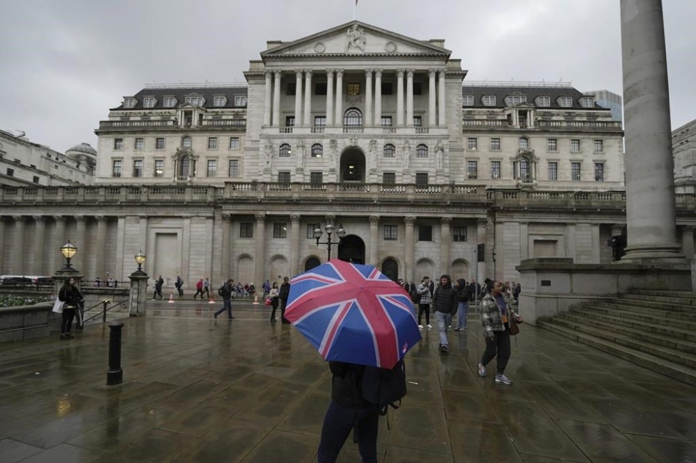 FILE - A woman with an umbrella stands in front of the Bank of England, at the financial district in London, Thursday, Nov. 3, 2022. From winemakers in California to startups across the Atlantic Ocean, companies are scrambling to figure out how to manage their finances after their bank, Silicon Valley Bank, suddenly shut down on Friday, March 10, 2023. The Bank of England said late Friday it would put Silicon Valley Bank UK in its insolvency procedure, which would pay out depositors up to a limit of 170,000 British pounds ($204,544) for joint accounts