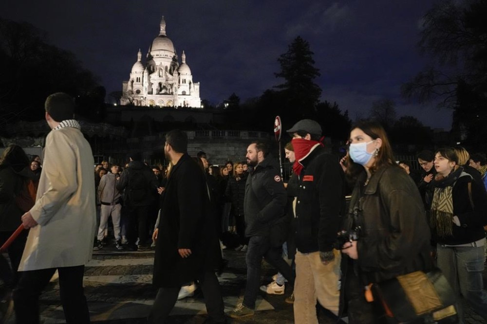 Protesters pass by the Montmartre Sacré-Coeur Basilica during a protest in Paris, Wednesday, March 22, 2023. Macron said Wednesday that the pension bill he pushed through without a vote in parliament needs to be implemented by the