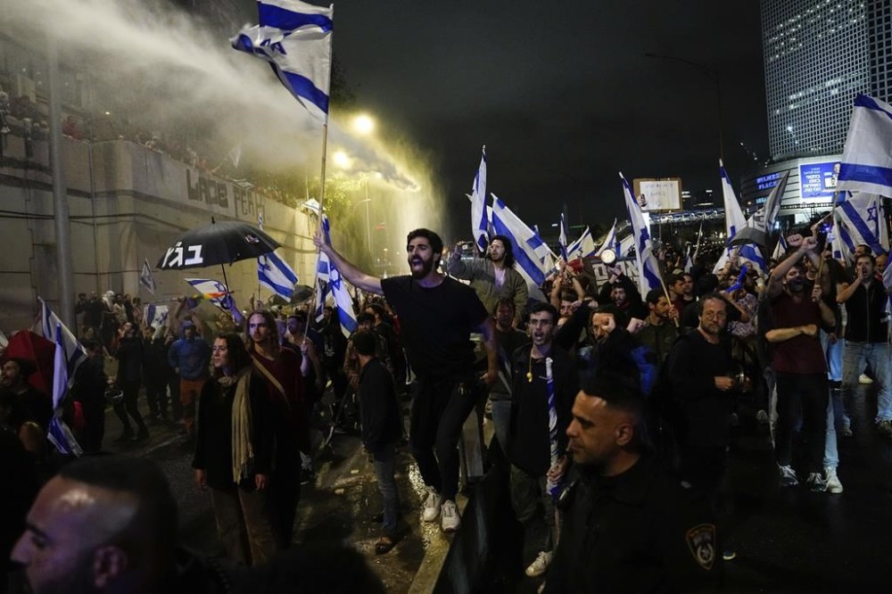 Israeli police use a water cannon to disperse demonstrators blocking the freeway during a protest against plans by Prime Minister Benjamin Netanyahu's government to overhaul the judicial system in Tel Aviv, Israel, Saturday, March 25, 2023. (AP Photo/Ariel Schalit)