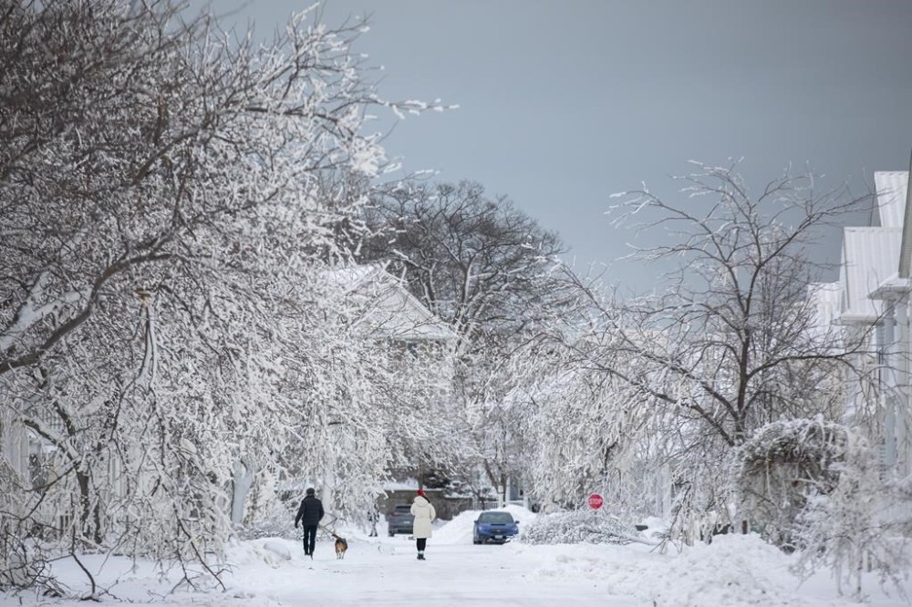 People walk along an ice covered street after a winter storm in Fort Erie, Ont., Tuesday, Dec. 27, 2022. Nearly two dozen small municipalities in Ontario will share $5.5 million to help with recovering from extreme weather. THE CANADIAN PRESS/Nick Iwanyshyn