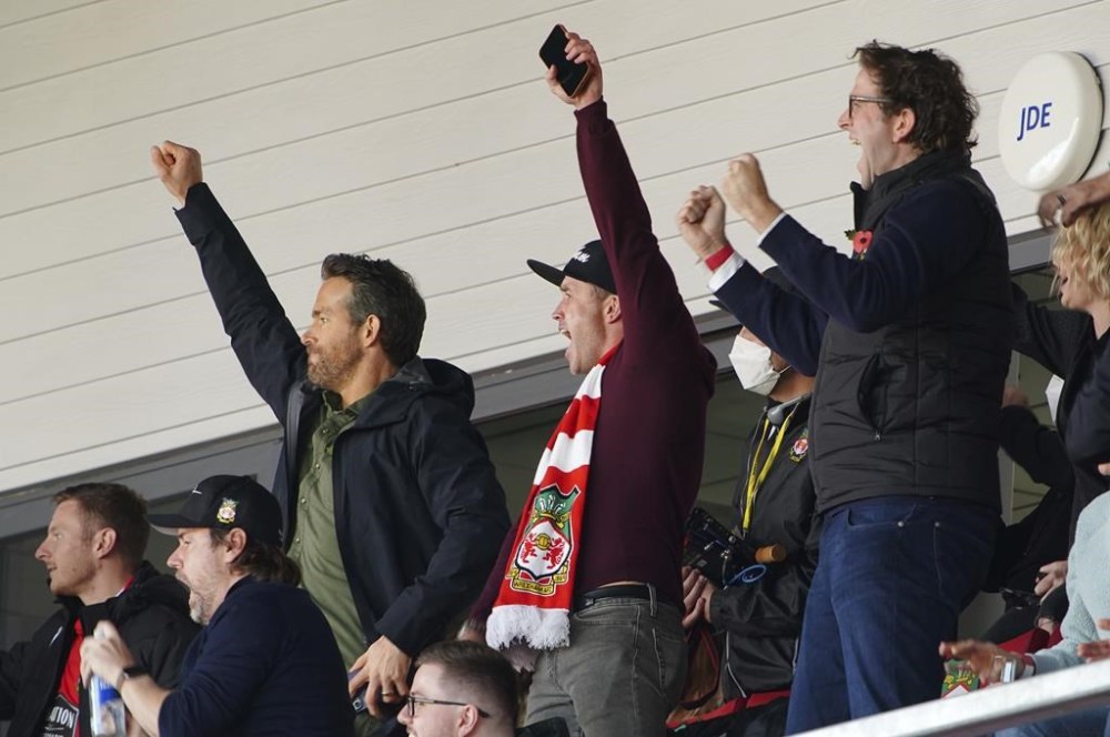 FILE - Wrexham owners, Ryan Reynolds, center left and Rob McElhenney, center, celebrate their side's first goal of the game, scored by Harry Lennon during the Vanarama National League match against Torquay United, at the Racecourse Ground, Wrexham, England, on Oct. 30, 2021. Soccer sensation Wrexham AFC is coming to America. The fifth-tier Welsh side, which has become a global fan favorite since Hollywood stars Reynolds and McElhenney bought it and then launched a documentary series,