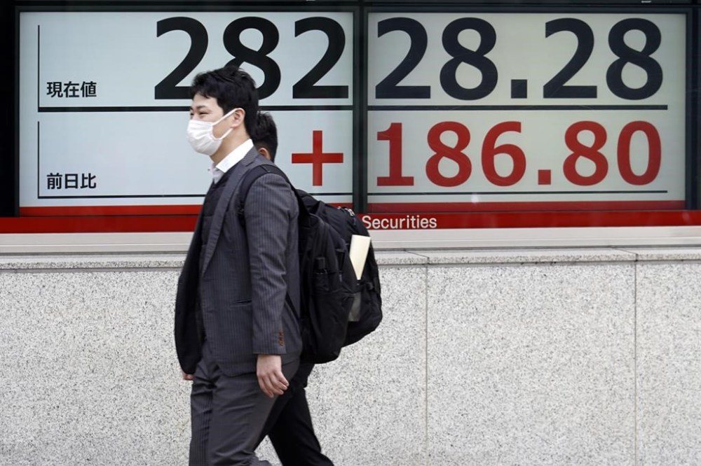 People walk in front of an electronic stock board showing Japan's Nikkei 225 index at a securities firm Monday, April 3, 2023, in Tokyo. Oil prices soared more than 5% after Saudi Arabia and other major oil producers said they will cut production by 1.15 million barrels per day from May until the end of the year. Shares in Asia were mixed on Monday and the dollar rose against the Japanese yen. (AP Photo/Eugene Hoshiko)