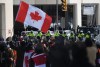 A person waves a Canadian flag as police on horseback and an armoured police vehicle are positioned in front of protesters, on the 22nd day of a protest against COVID-19 measures that has grown into a broader anti-government protest, in Ottawa, on Friday, Feb. 18, 2022. Lawyers for the federal attorney general are set to expand today on the legal rationale for the historic use of the Emergencies Act to dispel 