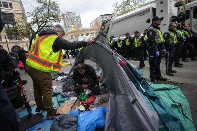 A man is seen inside his tent as police officers stand by while city workers clear an encampment on East Hastings Street in the Downtown Eastside of Vancouver, Wednesday, April 5, 2023. A handful of homeless people set up tents overnight along a stretch of Vancouver's Hastings Street that was cleared Wednesday in a co-ordinated effort by city officials and Vancouver police. THE CANADIAN PRESS/Darryl Dyck