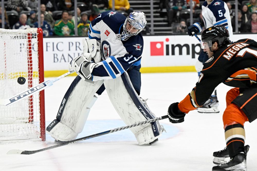 Winnipeg Jets goaltender Connor Hellebuyck, left, clears the puck against Anaheim Ducks' Jayson Megna during the third period. (AP Photo/Alex Gallardo)