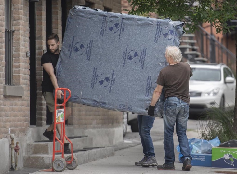 People carry a mattress into an apartment on moving day in Montreal, Friday, July 1, 2022. As moving season dawns, those looking to save money on the process have a truckload of options before them. THE CANADIAN PRESS/Graham Hughes