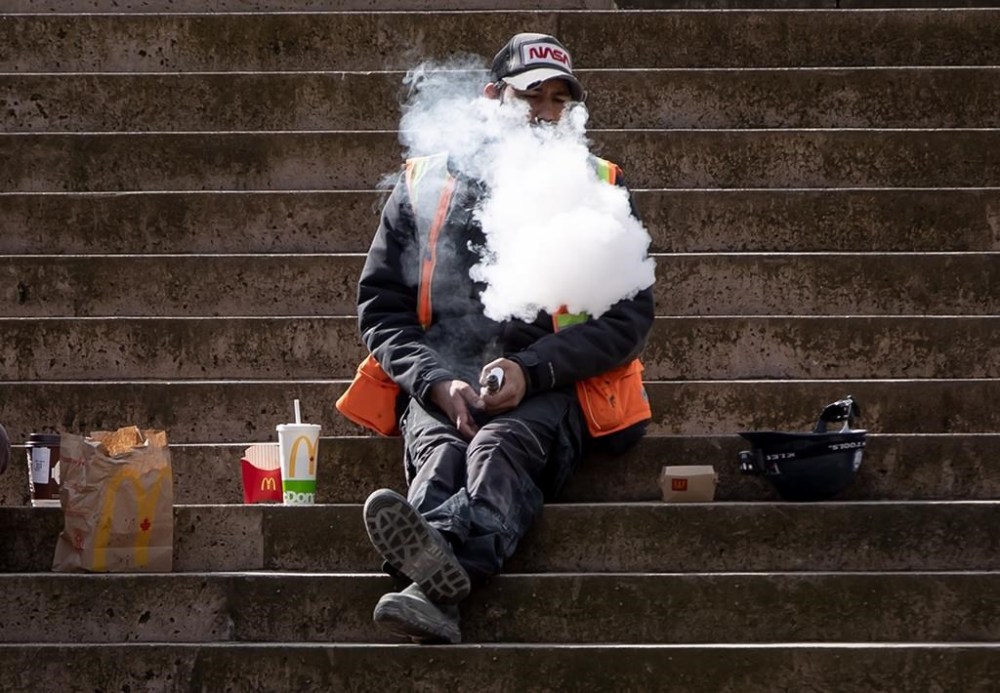A construction worker exhales after using a vaping device while eating lunch on the steps at Robson Square, in Vancouver, on Monday, March 8, 2021. The Quebec government is announcing its intention to modify the province's anti-tobacco law to crack down on vaping, including by banning the sale of flavoured products. THE CANADIAN PRESS/Darryl Dyck