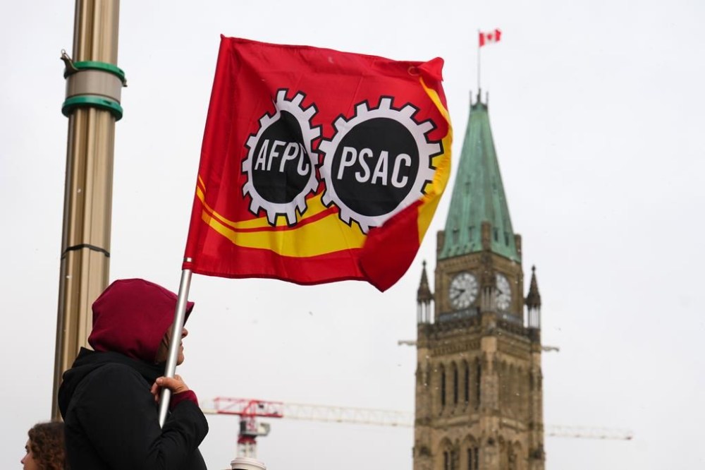 A PSAC worker holds a flag on a picket line in Ottawa, Wednesday, April 19, 2023. Canada's largest federal public-service union and the federal government remain at the bargaining table as workers strike and service disruptions begin to be felt across the country. THE CANADIAN PRESS/Sean Kilpatrick