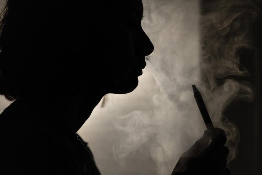 A person poses for a photograph as they vape in Melbourne, March 23, 2023. Recreational vaping will be banned as the government seeks to prevent the next generation of nicotine addicts, Australia's Health Minister Mark Butler said on Tuesday, May 2, 2023.(Diego Fedele/AAP Image via AP)