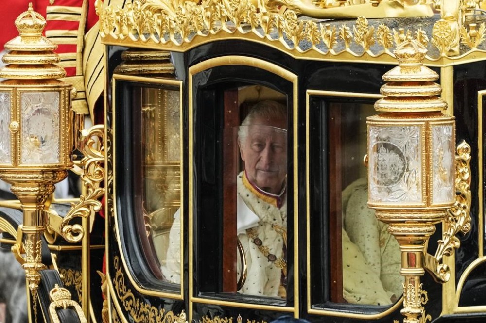 Britain's King Charles III is seen through the window of the Diamond Jubilee State Coach as he leaves Buckingham Palace with Camilla, the Queen Consort, for the coronation ceremony in London, Saturday, May 6, 2023. (AP Photo/Frank Augstein)
