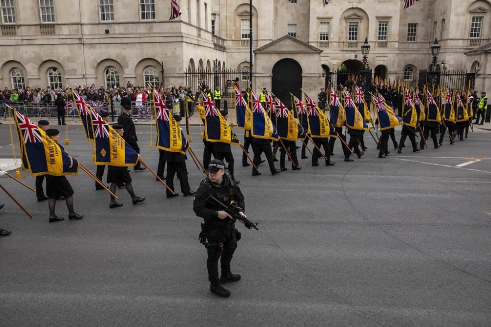 The Royal British Legion crosses the road to Horse Guards Parade under the watchful eye of an armed police officer during the coronation of King Charles III and Camilla, the Queen Consort, in London, Saturday, May 6, 2023. (Antonio Olmos/Pool Photo via AP)