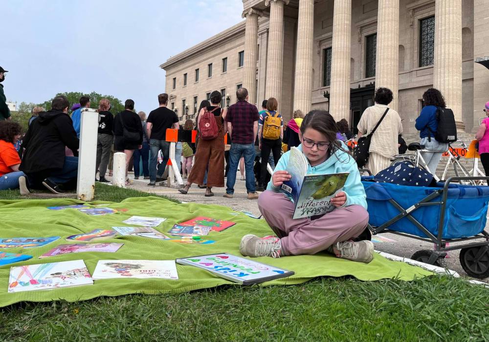 Grade 3 student Margot McNabb reads a picture book at a Winnipeg rally Tuesday in solidarity with opponents of book bans. (Maggie MacIntosh / Winnipeg Free Press)