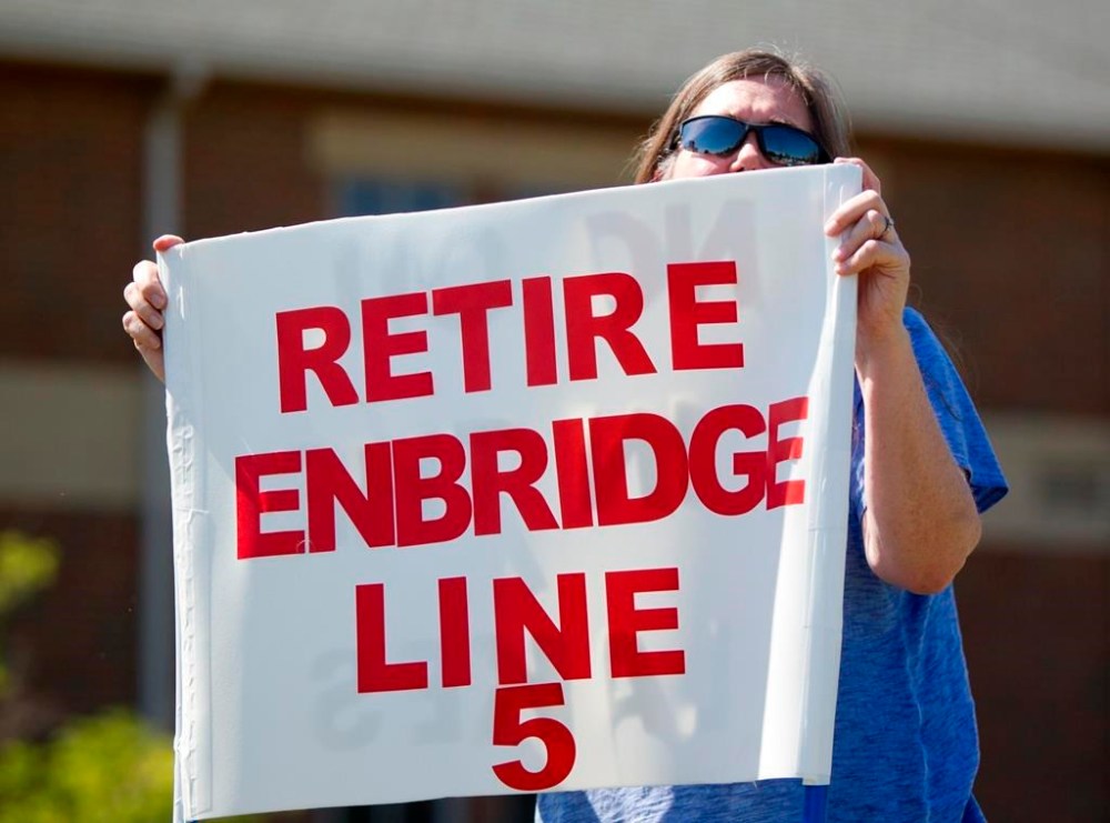 In this July 6, 2017, file photo, Lauren Sargent takes part in a protest before the Enbridge Line 5 pipeline public information session in Holt, Mich. The controversial Canada-U.S. oil and gas conduit could be facing its toughest challenger yet: rapid erosion in the very watershed the pipeline’s detractors are trying to protect. THE CANADIAN PRESS/Cory Morse-The Grand Rapids Press via AP