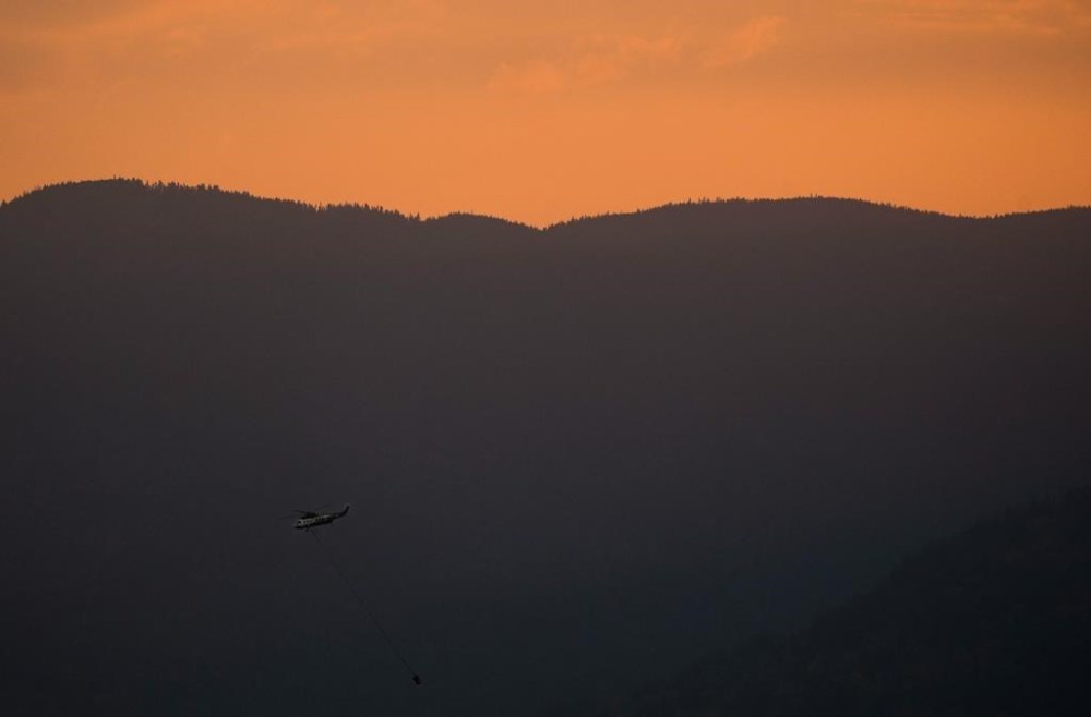 A change in wind direction and 48 firefighters battling overnight has kept two out-of-control wildfires from advancing closer to Fort St. John in northeast British Columbia. A helicopter with a water bucket battling the Flood Falls Trail wildfire picks up water from the Fraser River, in Hope, B.C., Monday, Sept. 12, 2022. THE CANADIAN PRESS/Darryl Dyck