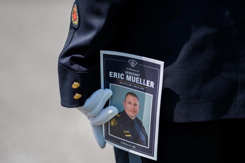 A member of the Ontario Provincial Police holds a program during the funeral of Ontario Provincial Police Sgt. Eric Mueller in Ottawa, on Thursday, May 18, 2023. Sgt. Mueller was killed in the line of duty while responding to call on May 11 in the village of Bourget, Ont. The lawyers for a man accused of killing the Ontario Provincial Police officer and injuring two others are disputing the characterization of the shooting as an ambush. THE CANADIAN PRESS/Spencer Colby