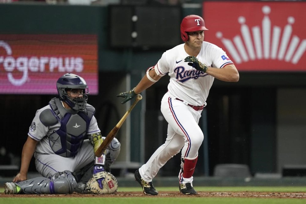 Texas Rangers' Nathaniel Lowe, right, hits a single in front of Colorado Rockies catcher Elias Diaz scoring Rangers' Marcus Semien during the first inning of a baseball game in Arlington, Texas, Saturday, May 20, 2023. (AP Photo/LM Otero)