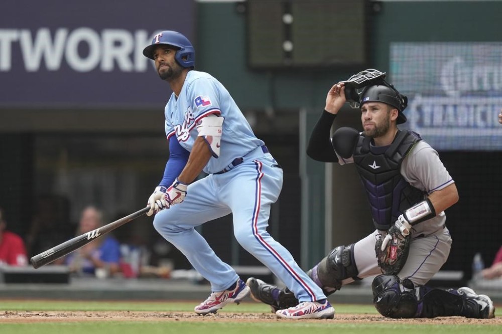 Texas Rangers' Marcus Semien, left, and Colorado Rockies catcher Austin Wynns watch Semien's double fly away into the outfield scoring two runs during the second inning of a baseball game in Arlington, Texas, Sunday, May 21, 2023. Rangers Ezequiel Duran and Leody Taveras scored on the play. (AP Photo/LM Otero)