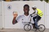 A cyclist rides past a poster of Real Madrid's Vinicius Junior outside the Santiago Bernabeu stadium in Madrid, Spain, Monday, May 22, 2023. Spanish soccer is again embroiled in a racism debate after yet another case of abuse against Real Madrid forward Vinicius Junior, with the president of Spain's soccer federation acknowledging that the country has a racism problem and the player's club asking authorities to investigate the latest incident as a hate crime. (AP Photo/Paul White)