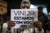 A woman holds a sign with a message that reads in Portuguese; 