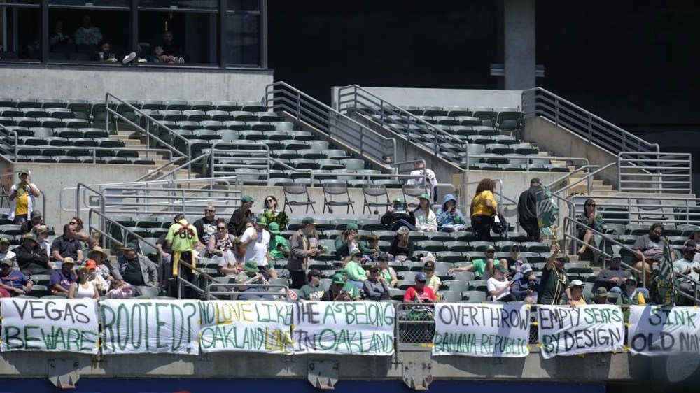Fans watch from behind signs hanging in right field during the fifth inning of a baseball game between the Oakland Athletics and the Houston Astros in Oakland, Calif., Saturday, May 27, 2023. (AP Photo/Jeff Chiu)