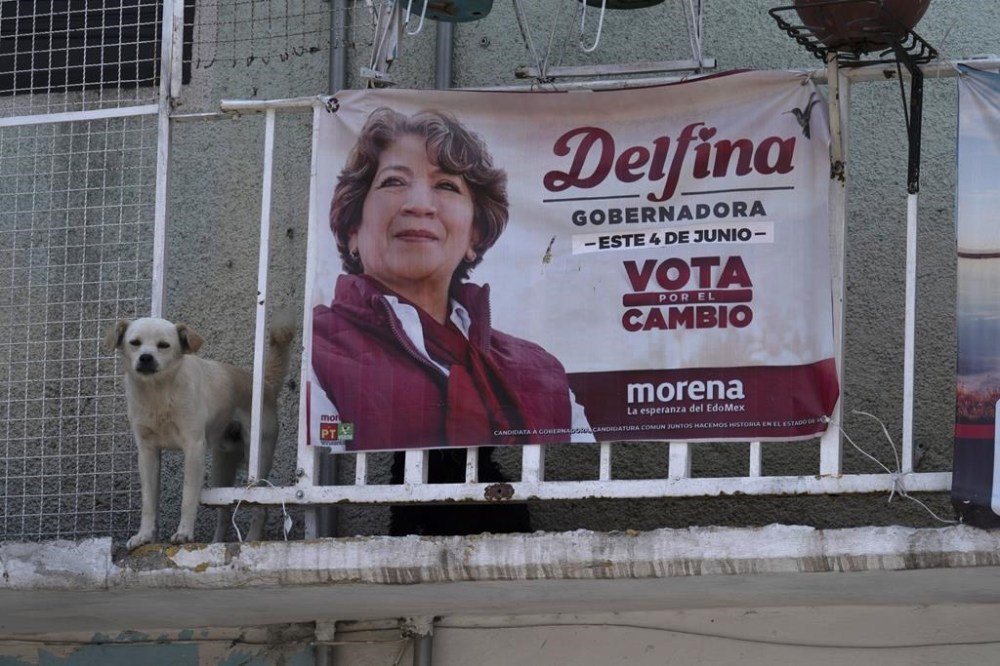 A dog stands next to an electoral banner promoting MORENA gubernatorial candidate Delfina Gomez, in Nezahualcoyotl, Mexico, Saturday, May 27, 2023. Voters in Mexico state go to the polls on June 4 to elect a new governor.(AP Photo/Marco Ugarte)