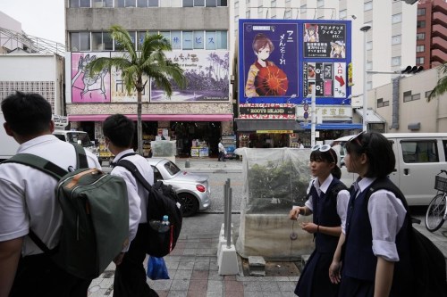 School children walk past plants covered with a net placed in preparation for Typhoon Mawar in Naha, southern Japan, Wednesday, May 31, 2023, as it was moving towards the Okinawa islands. (AP Photo/Hiro Komae)