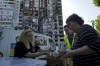 Local residents get free meals from volunteers against the background of their apartment house, damaged in the Russian rocket attack, in Kharkiv, Ukraine, Friday, June 2, 2023. (AP Photo/Andrii Marienko)
