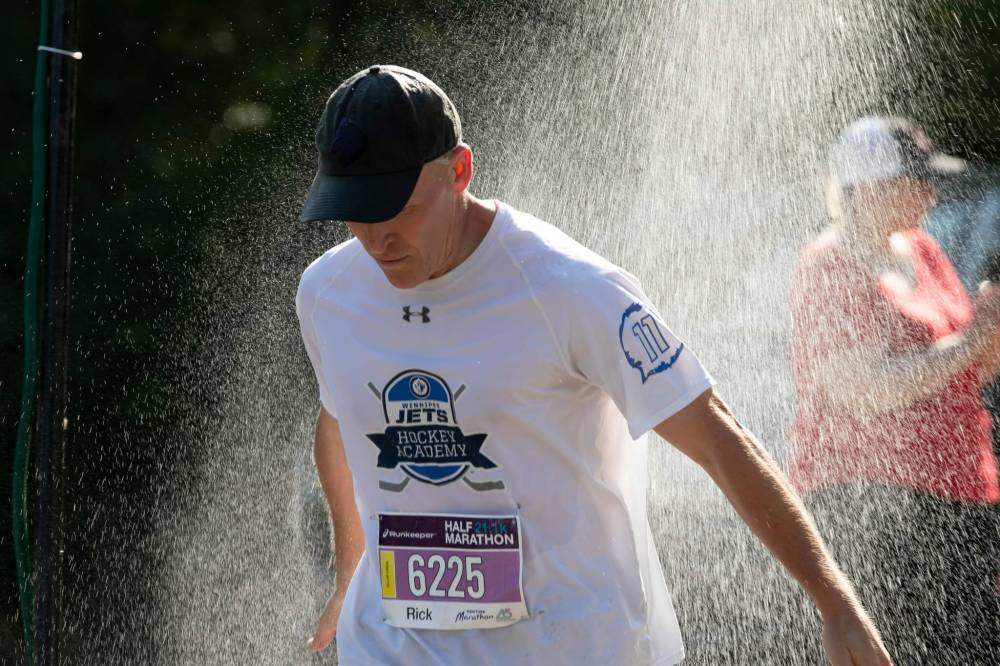 BROOK JONES / WINNIPEG FREE PRESS
Rick Bochinski runs under a makeshift shower at a volunteer water station run by Eastman Flames U14 and U16 ringette teams near Crescent Drive Park, while competing in the Half Marathon.