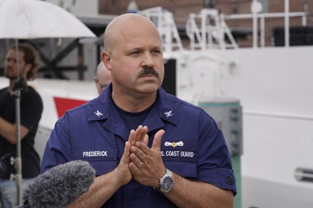 U.S. Coast Guard Capt. Jamie Frederick, front, faces reporters during a news conference, Tuesday, June 20, 2023, at Coast Guard Base Boston, in Boston. The U.S. Coast Guard says a search covering 10,000 square miles (26,000 square kilometers) has turned up no signs of a missing submersible off New England. Authorities made the announcement Tuesday. (AP Photo/Steven Senne)