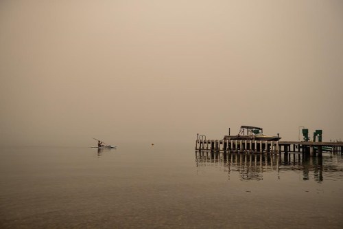 Thick smoke from wildfires blankets the area as a woman sits on a paddleboard on Okanagan Lake, in Lake Country, B.C., Friday, Aug. 13, 2021.&nbsp;Mounties in Kelowna, B.C., say they're assisting with the evacuation of a residential area due to a wildfire on Knox Mountain near Okanagan Lake.&nbsp;THE CANADIAN PRESS/Darryl Dyck