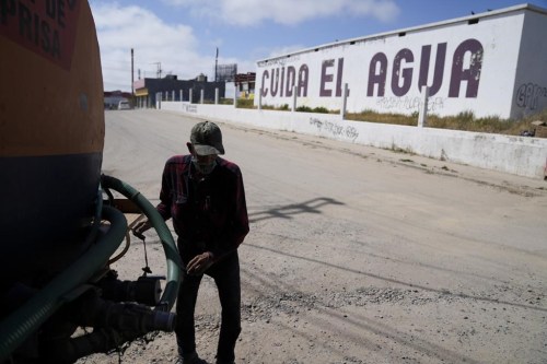 Augustin Rodriguez gets hoses ready on the back of his water truck as he delivers at a home across the street from a large sign that reads 