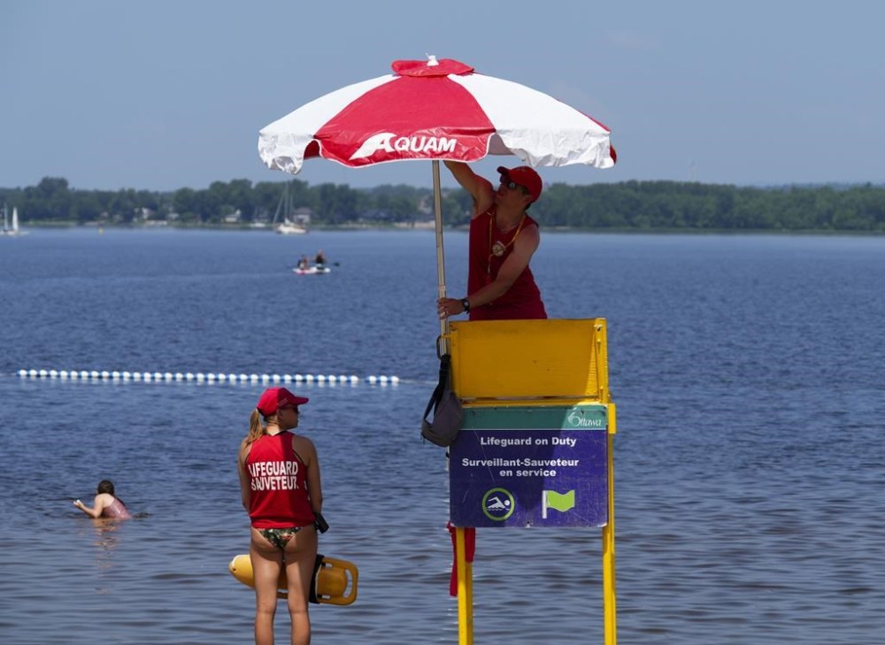 A lifeguard raises an umbrella as another continues to watch on at Britannia Beach as people take to the waters and shores of the Ottawa River in Ottawa on Tuesday, July 4, 2023. Wednesday could become the third straight day Earth unofficially marks a record-breaking high, the latest in a series of climate-change extremes that alarm but don't surprise scientists. THE CANADIAN PRESS/Sean Kilpatrick
